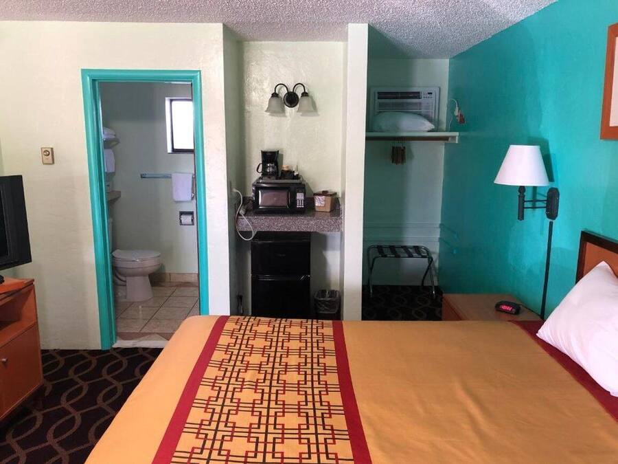 A hotel room with a bed, a desk with a computer, a microwave, a coffee maker, a lamp, and a view of the bathroom.