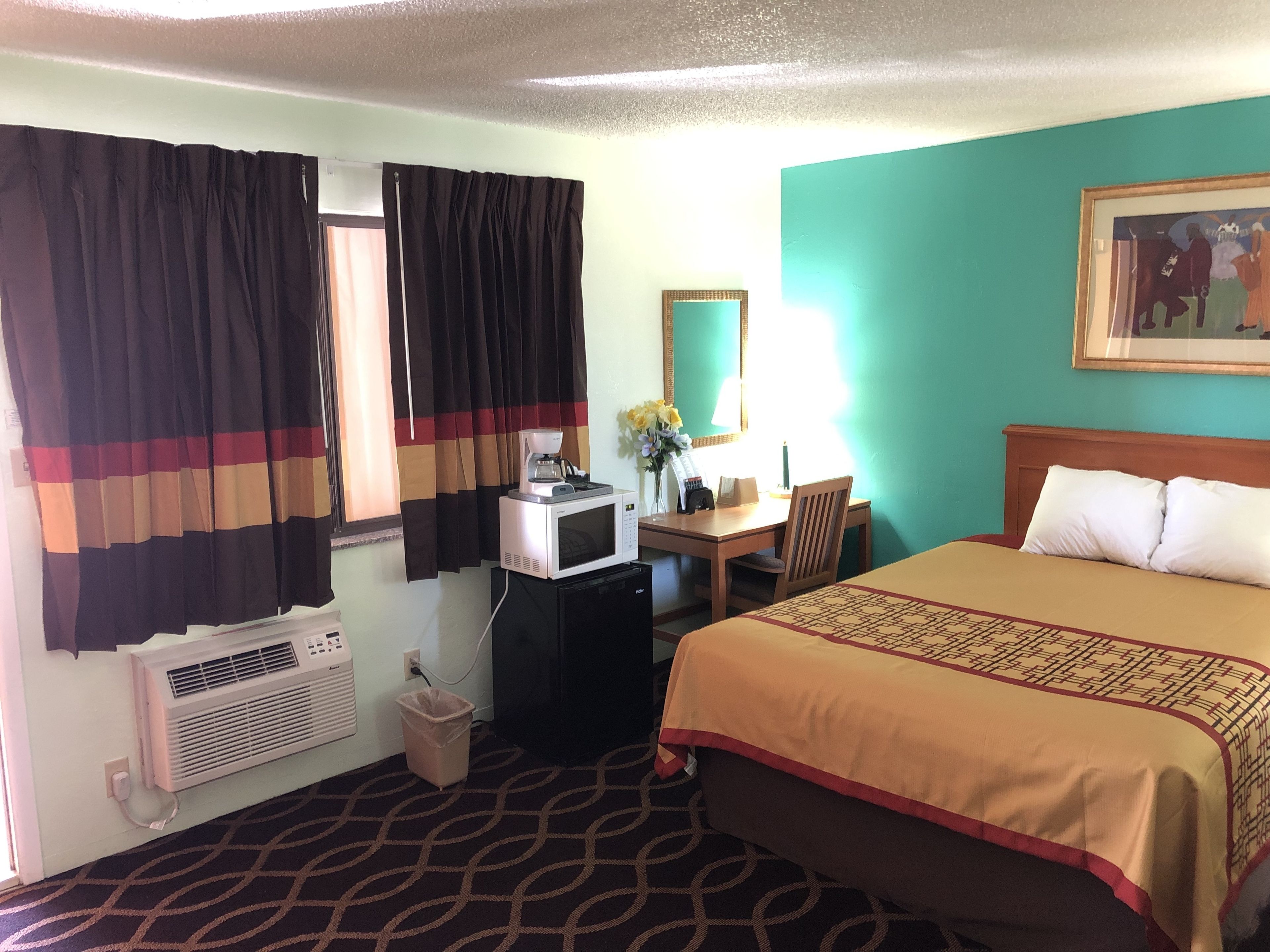 Habitación de hotel con cama, escritorio con silla, microondas, teléfono y ventana con cortinas.