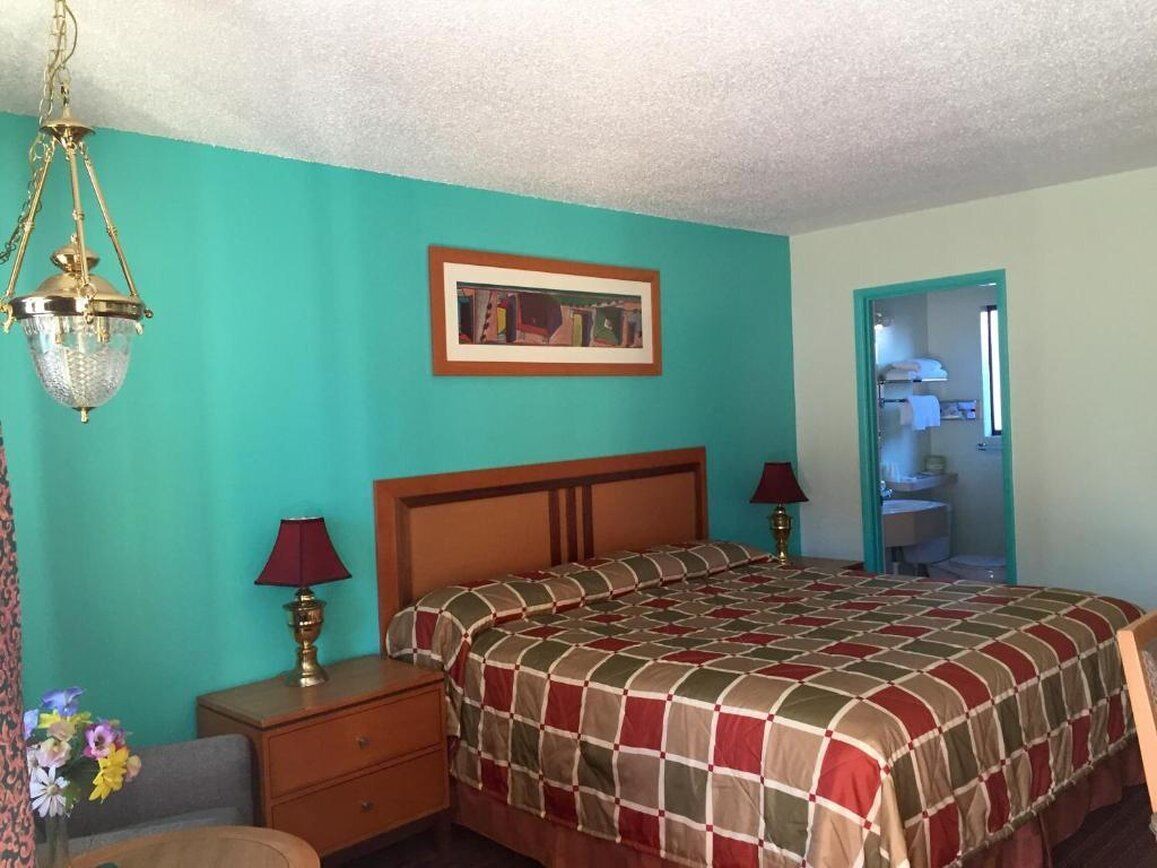 A bedroom with a bed, bedside tables, a lamp, a framed picture, and a door leading to a bathroom.