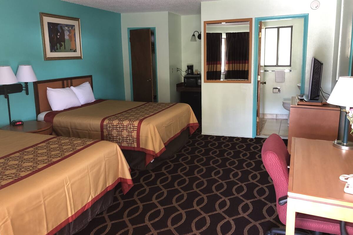 A hotel room with two beds, a desk, a chair, a television, and a bathroom visible through an open door.