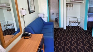 Habitación de hotel con un sofá azul, un escritorio de madera con un teléfono, un espejo, un microondas y un baño visible a través de una puerta abierta.