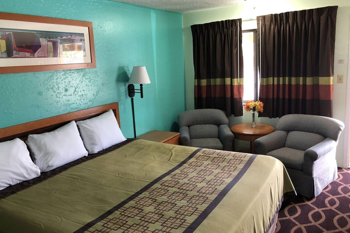 A hotel room with a bed, two armchairs, a small table with a vase of flowers, and a painting on the wall.