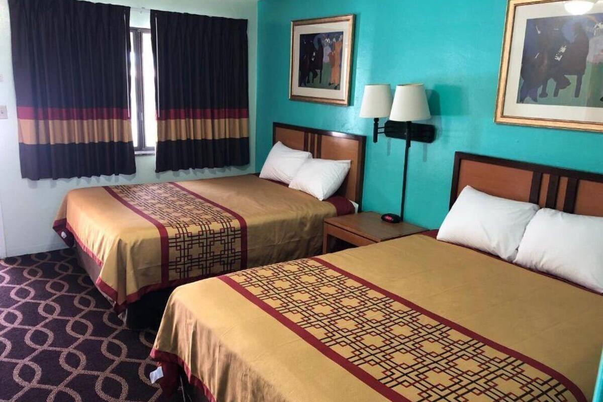 A hotel room with two beds, a nightstand, a lamp, and a window with curtains.