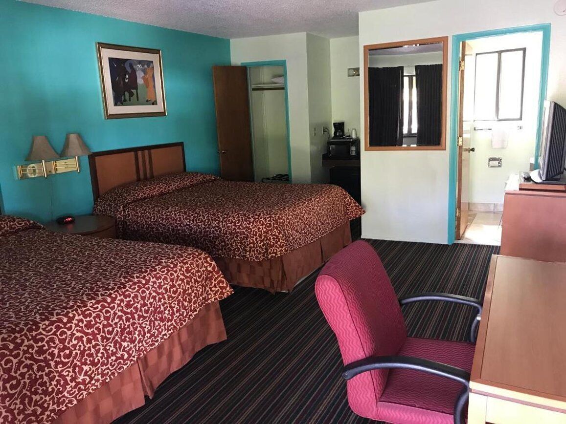 A hotel room with two beds, a desk, a chair, a wardrobe, and a painting on the wall.