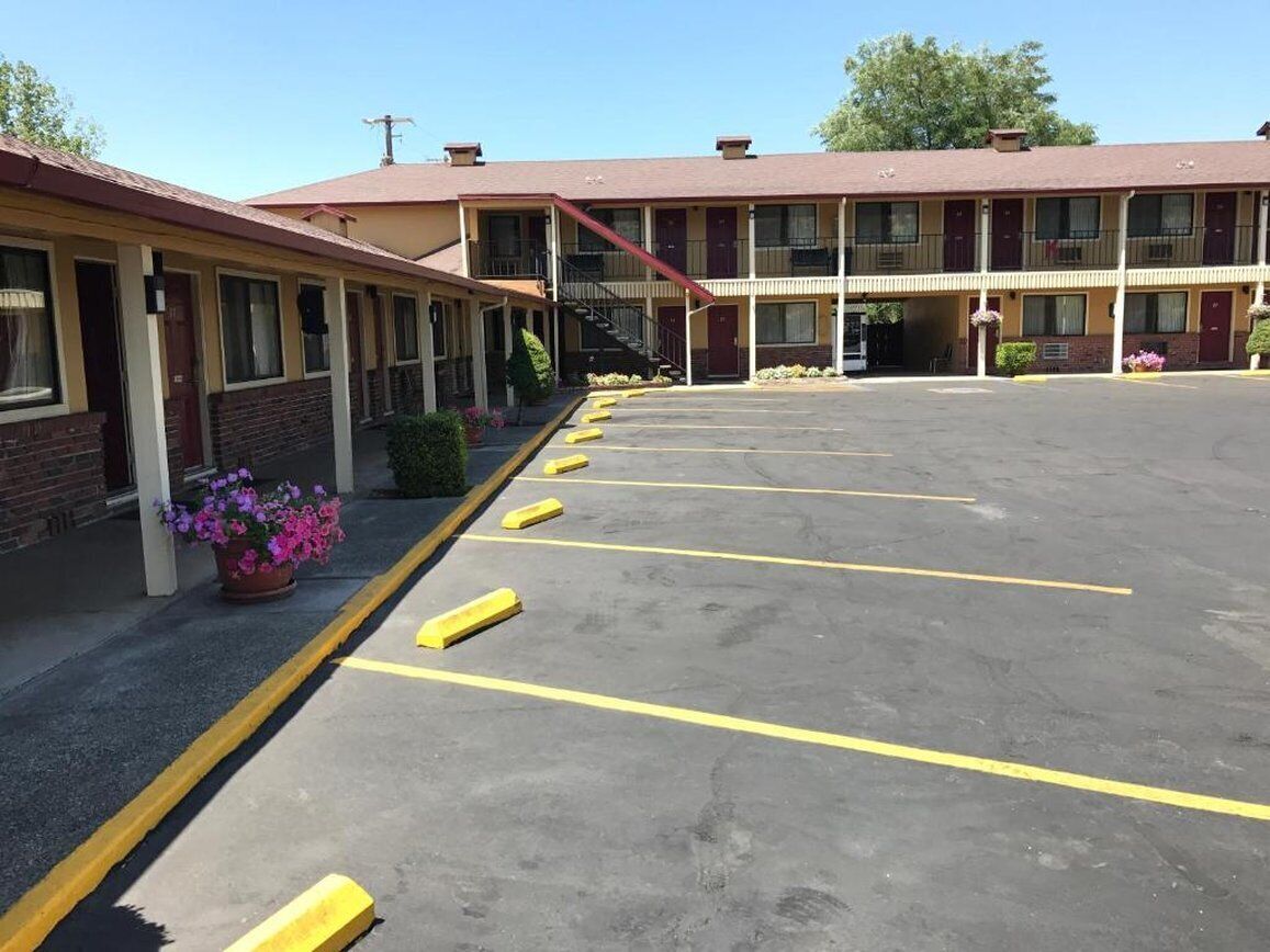 Un motel con estacionamiento, un corredor cubierto y un edificio con múltiples ventanas y puertas.