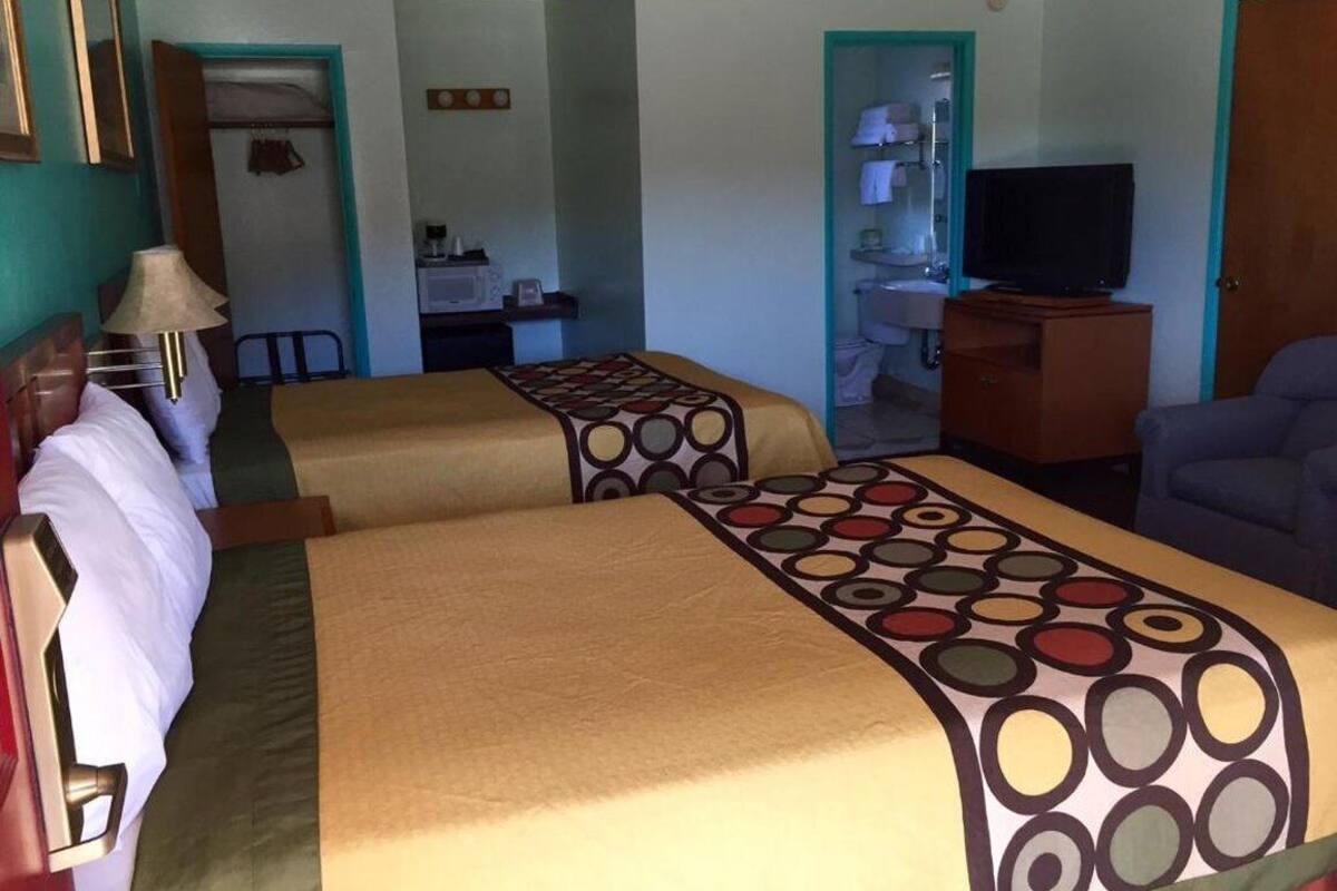 A hotel room with two beds, a TV, a desk, and a bathroom visible through an open door.