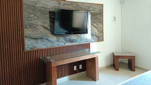 Una sala moderna con un televisor de pantalla plana montado en una pared de aspecto marmolizado, una mesa de centro de cristal y un banco de madera.