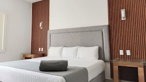 Una habitación de hotel moderna con una cama grande, una mesa de vidrio y paneles de madera en las paredes.