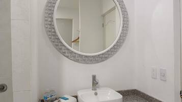 Un baño con un espejo redondo, un lavabo blanco y un perchero con toallas dobladas.