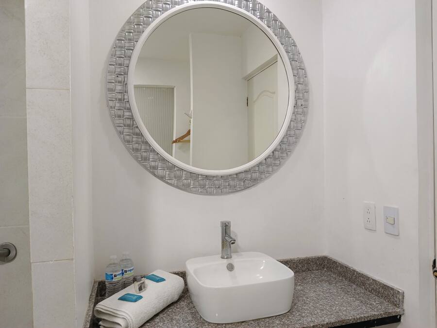 Un baño con un espejo redondo, un lavabo blanco y un perchero con toallas dobladas.
