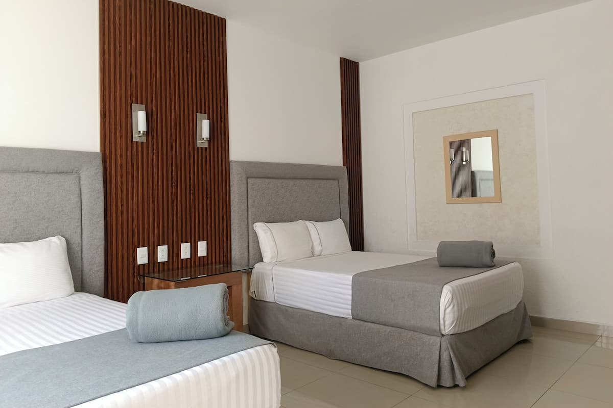 Habitación de hotel con dos camas, paneles de madera, un espejo y una mesita de noche con lámpara.