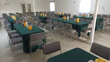Un salón de conferencias con varias mesas y sillas, equipado con botellas de agua y vasos.