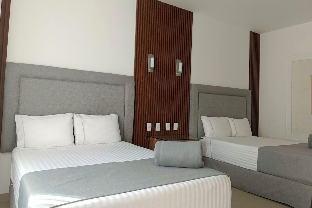 Hotellihuone, jossa on kaksi sänkyä, puupanelilla verhoiltu seinä ja pieni pöytä.