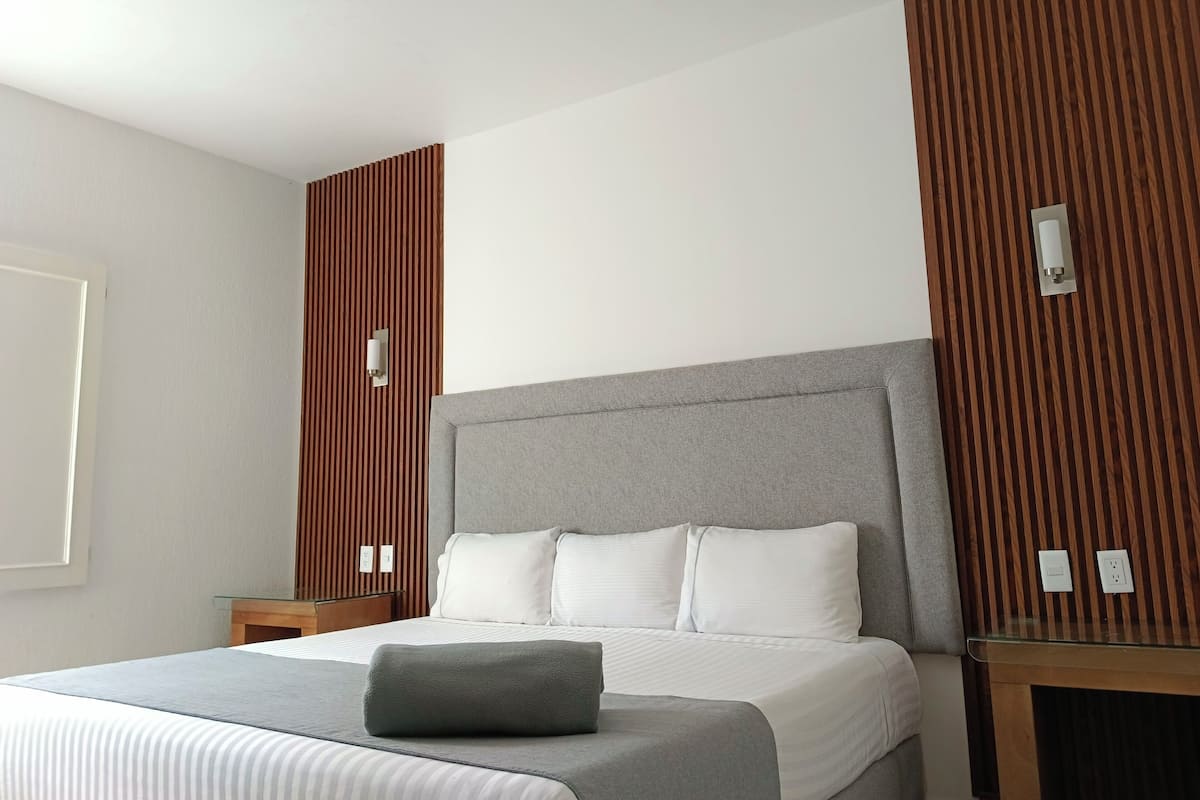Una habitación de hotel moderna con una cama grande, un muro decorativo de madera y una mesita de vidrio.