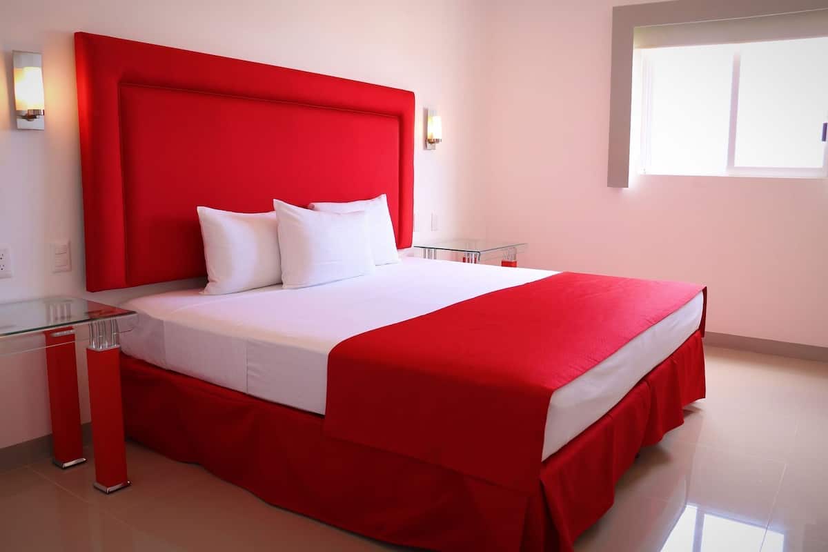 Una habitación de hotel moderna con cabecera roja, ropa de cama blanca y mesita de noche de vidrio.