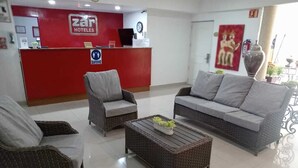 Zona de recepción de hotel con mobiliario de mimbre, un mostrador y un reloj.