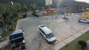 Un estacionamiento con una camioneta blanca, un camión y varios coches. Hay bolardos naranjas a lo largo de las líneas de aparcamiento.