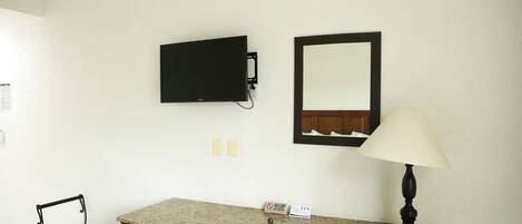 A room with a table, two chairs, a television mounted on the wall, a mirror, and a lamp.