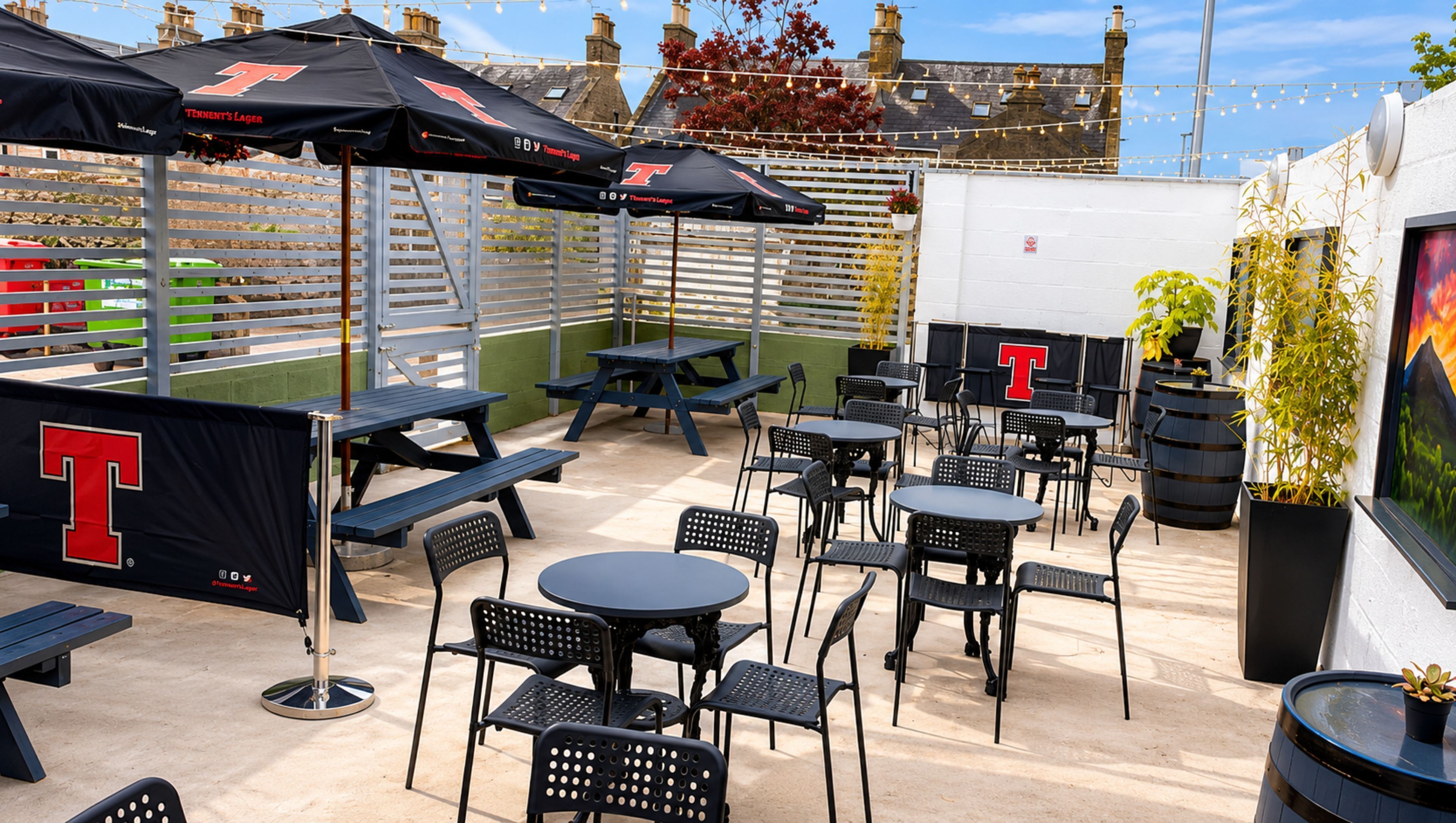 Ein Außenbereich mit einer Terrasse, Tischen, Stühlen und Sonnenschirmen. Ein großes T-Logo ist auf einem Banner zu sehen.