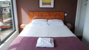 A hotel room with a large bed, a window with a view, a bedside table with a phone, and a painting on the wall.