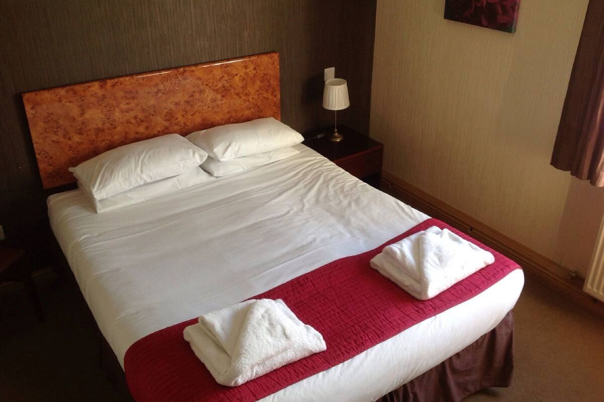 A neatly made bed with white linens, a red blanket, and two folded towels.