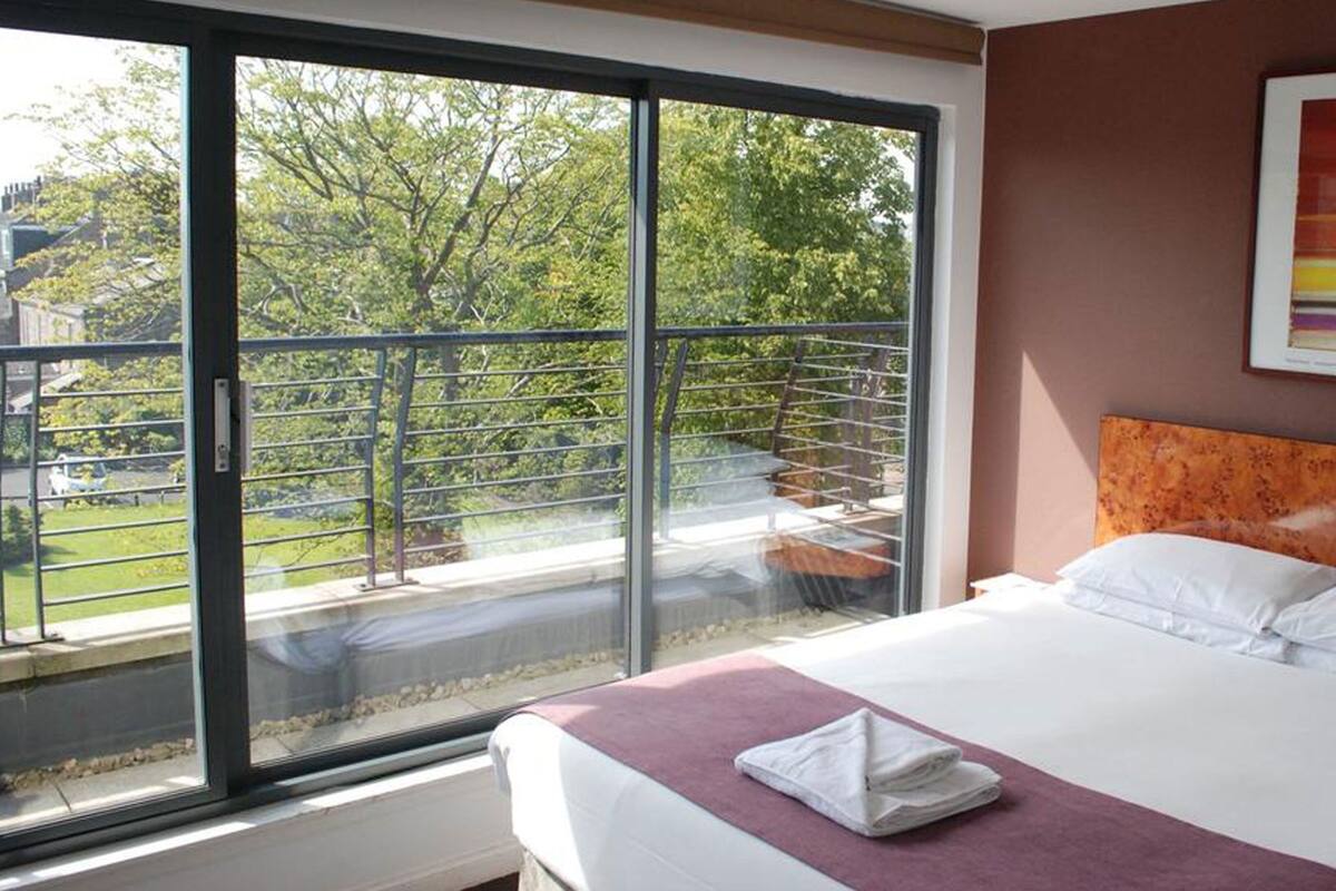 A hotel room with a large sliding glass door leading to a balcony, a bed with white linens, and a framed picture on the wall.