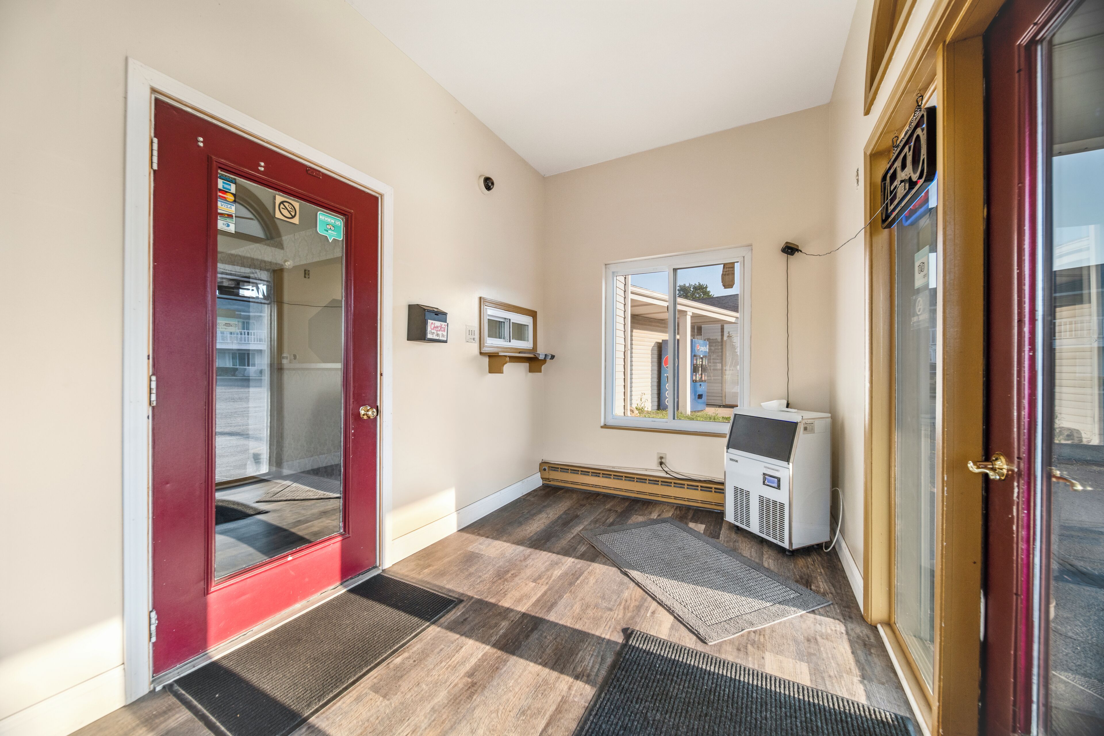 A hotel entrance with a red door, a thermostat, a window, and a wall-mounted sign.