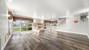 Ein geräumiges Wohnzimmer mit Kamin, großen Fenstern und einer Treppe, die zu einer weiteren Ebene führt.