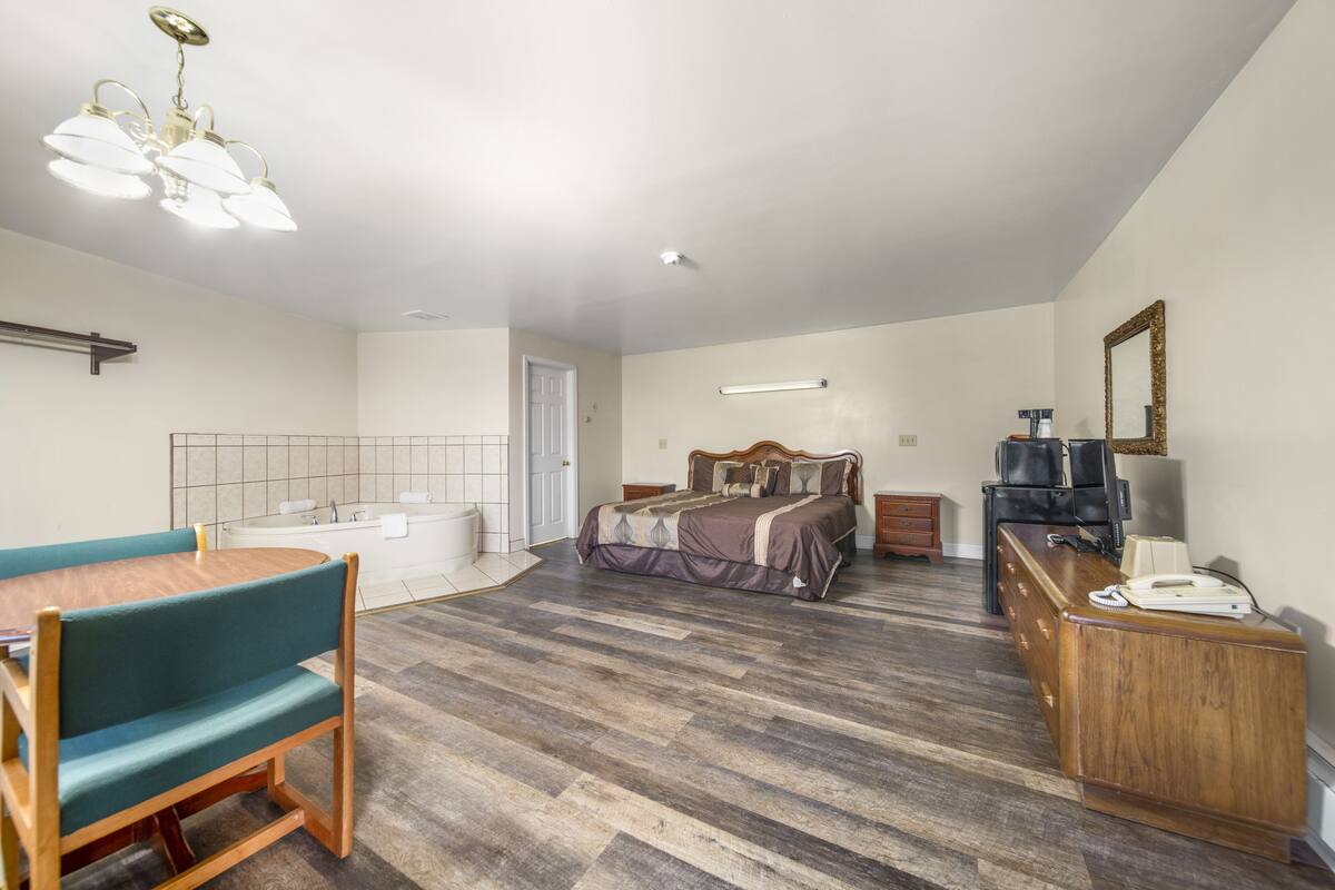 Une pièce comprenant une table à manger en bois, un banc, un lit avec une tête de lit, un bureau avec un téléphone et un miroir au mur.