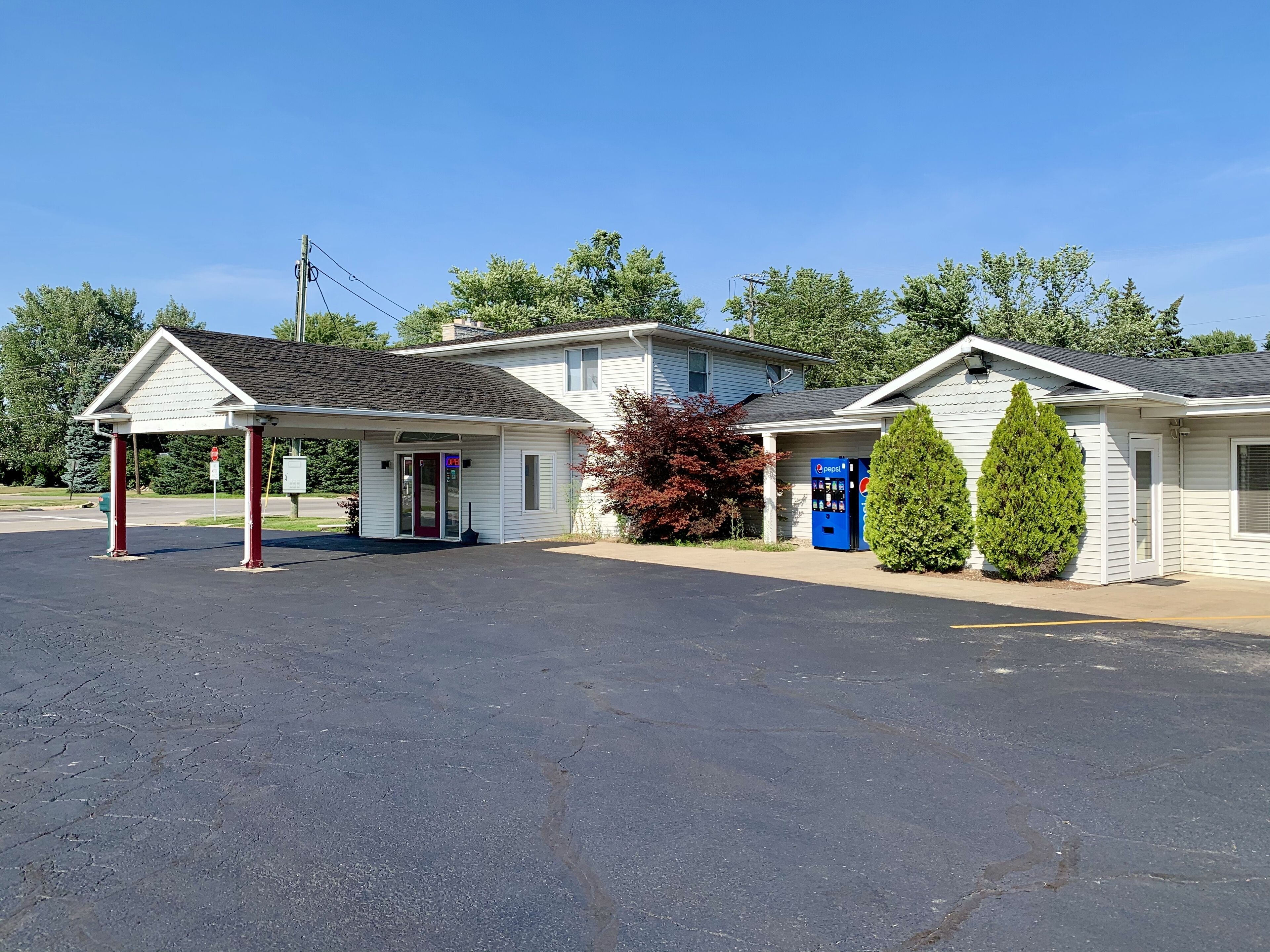 Un motel doté d’un parking couvert, d’un bâtiment à un seul étage et d’un distributeur de boissons Pepsi bien visible.