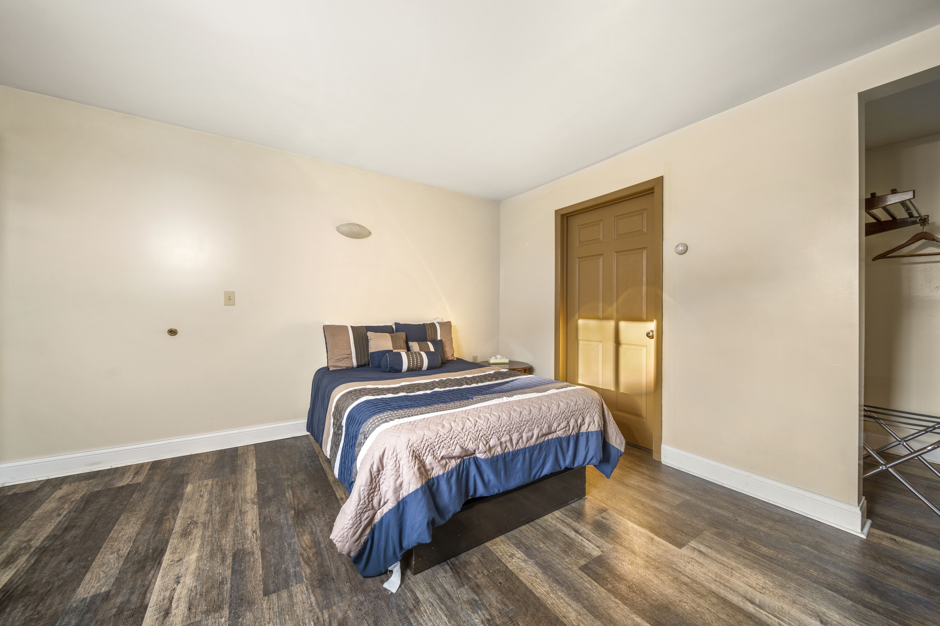 A bedroom with a large bed, wooden flooring, and a door leading to another room.