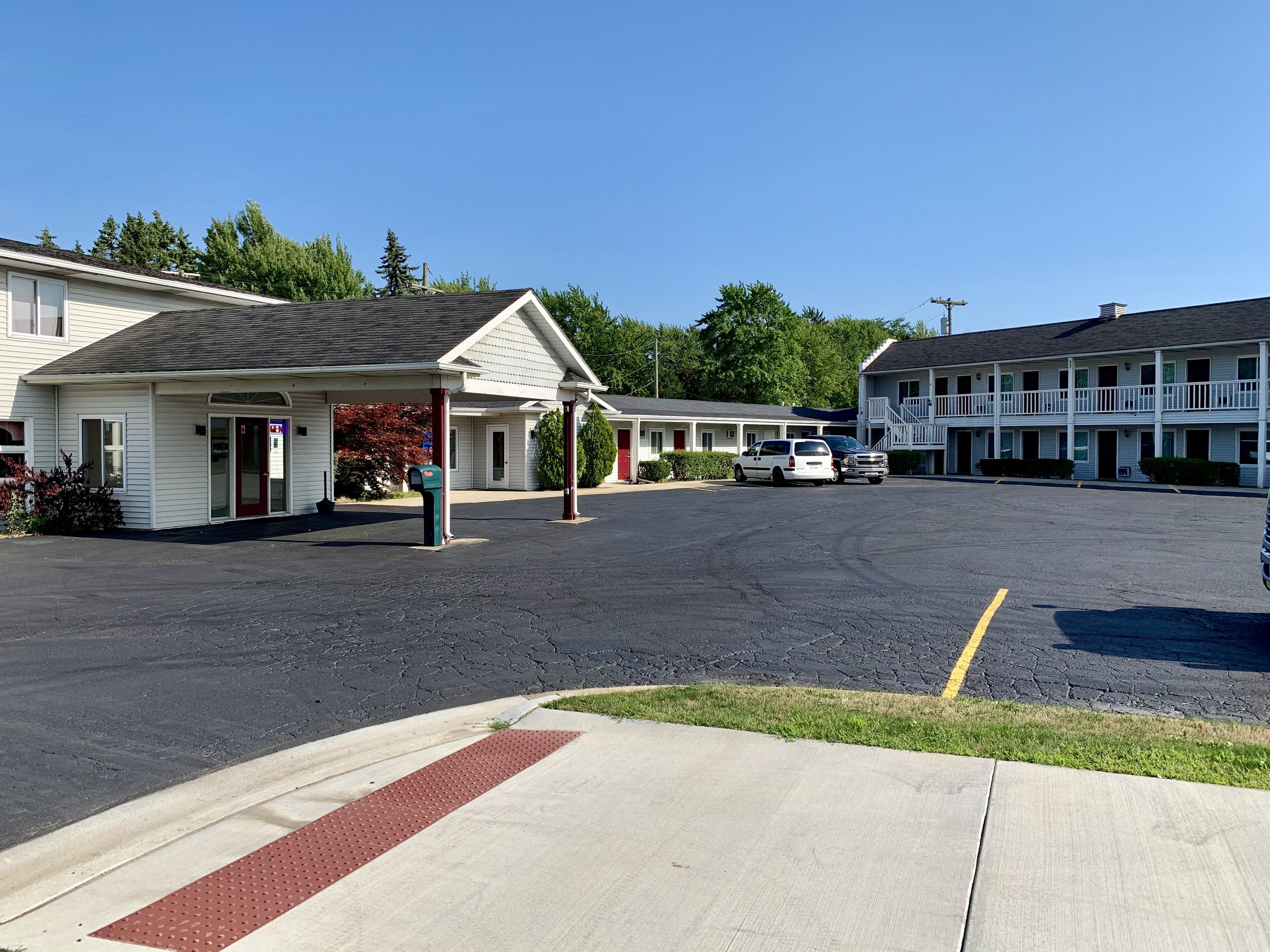 A motel with a covered parking area, multiple rooms, and a two-story building with a balcony.