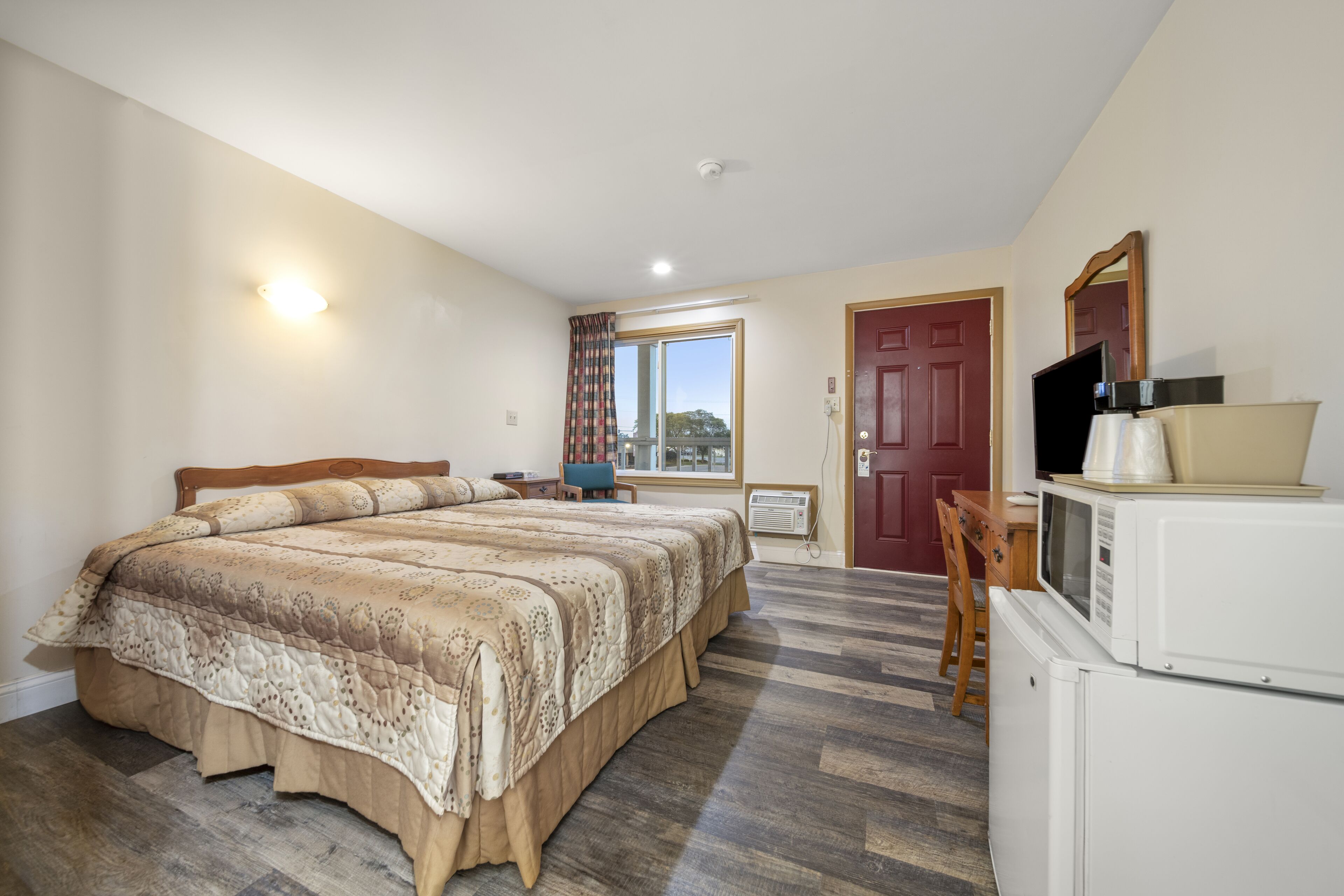 Une chambre avec un grand lit, une télévision, un four à micro-ondes et une fenêtre avec des rideaux.