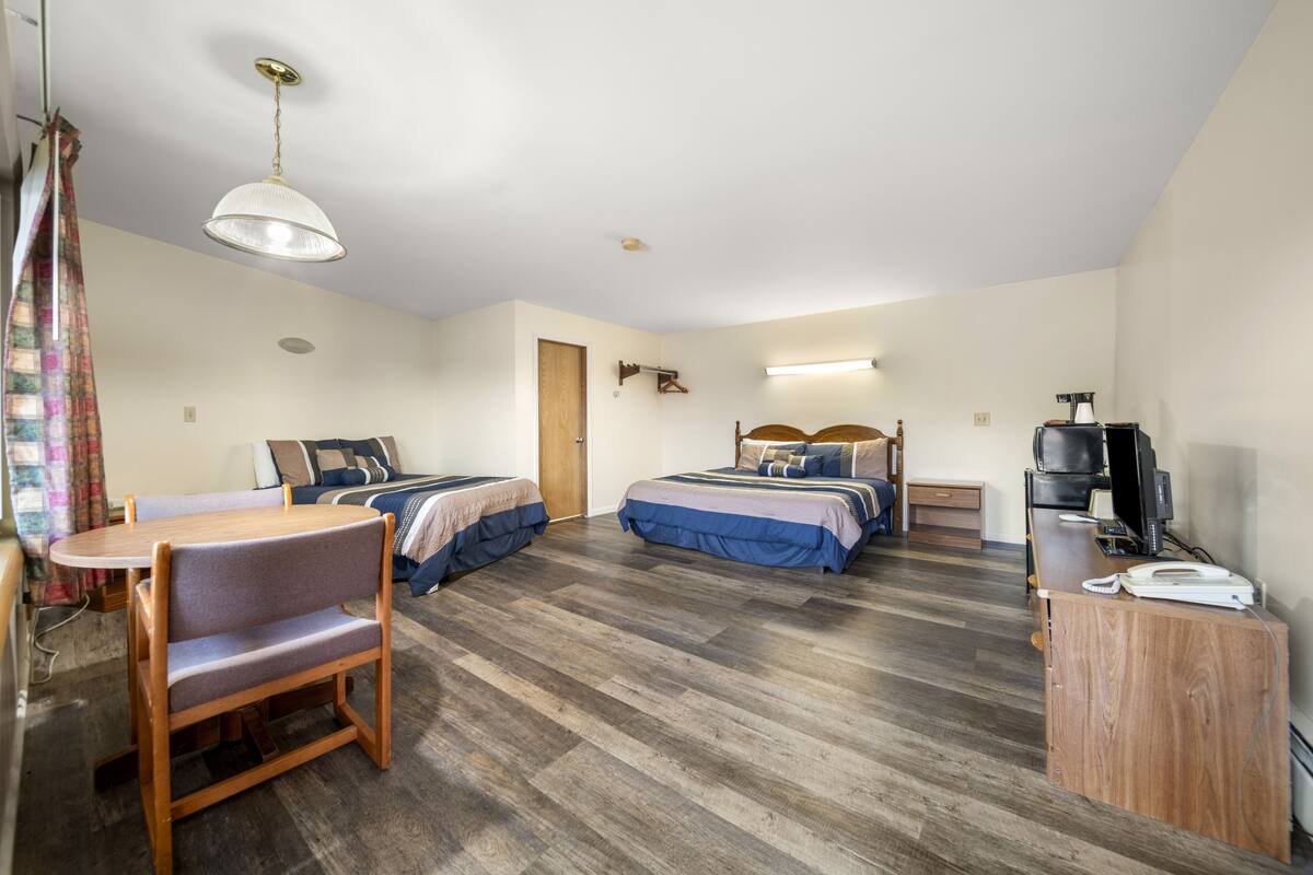 Une chambre d’hôtel avec deux lits, un bureau, une chaise, une télévision et une lampe.