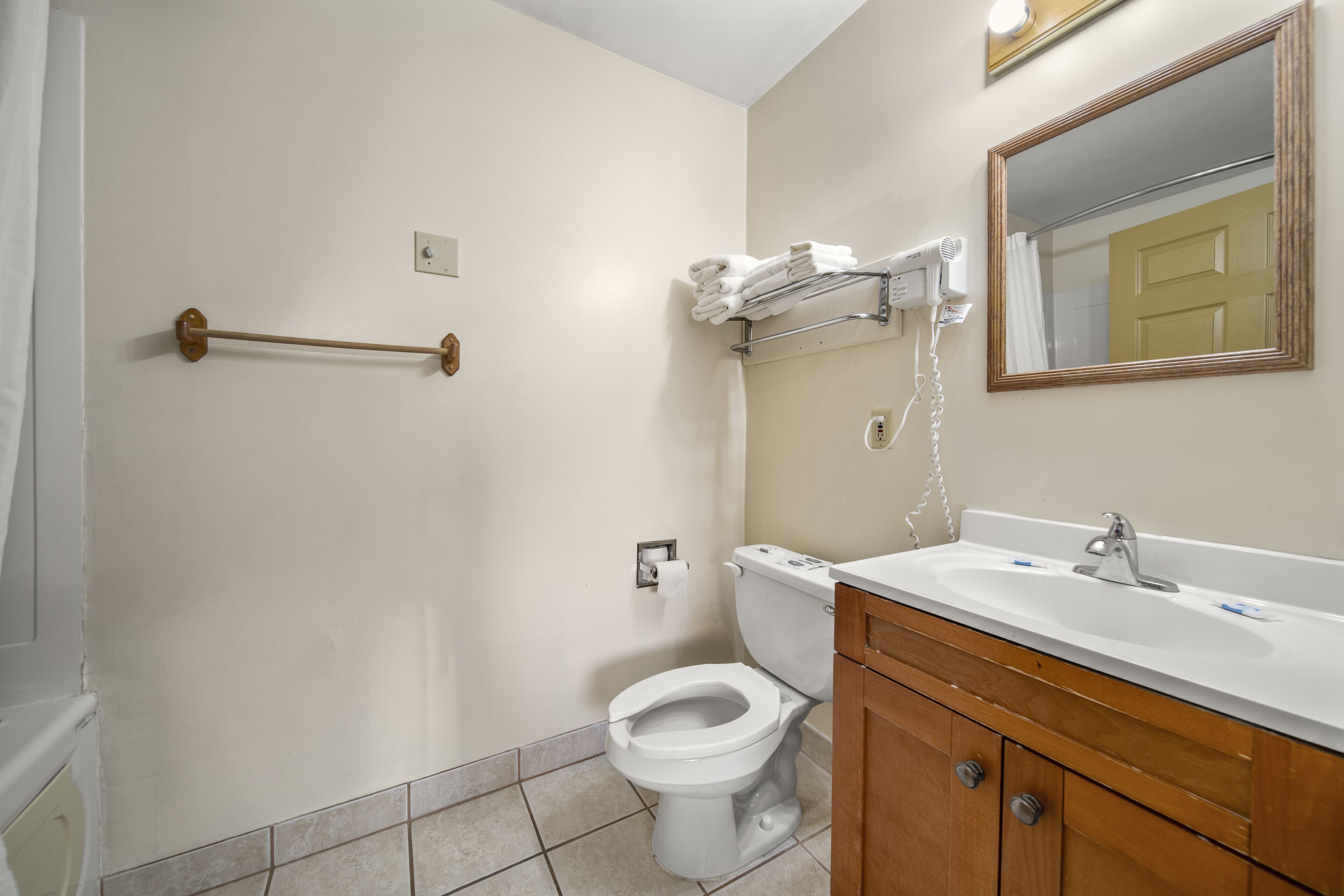 Une salle de bain avec des toilettes blanches, un lavabo, un miroir et un porte-serviettes.