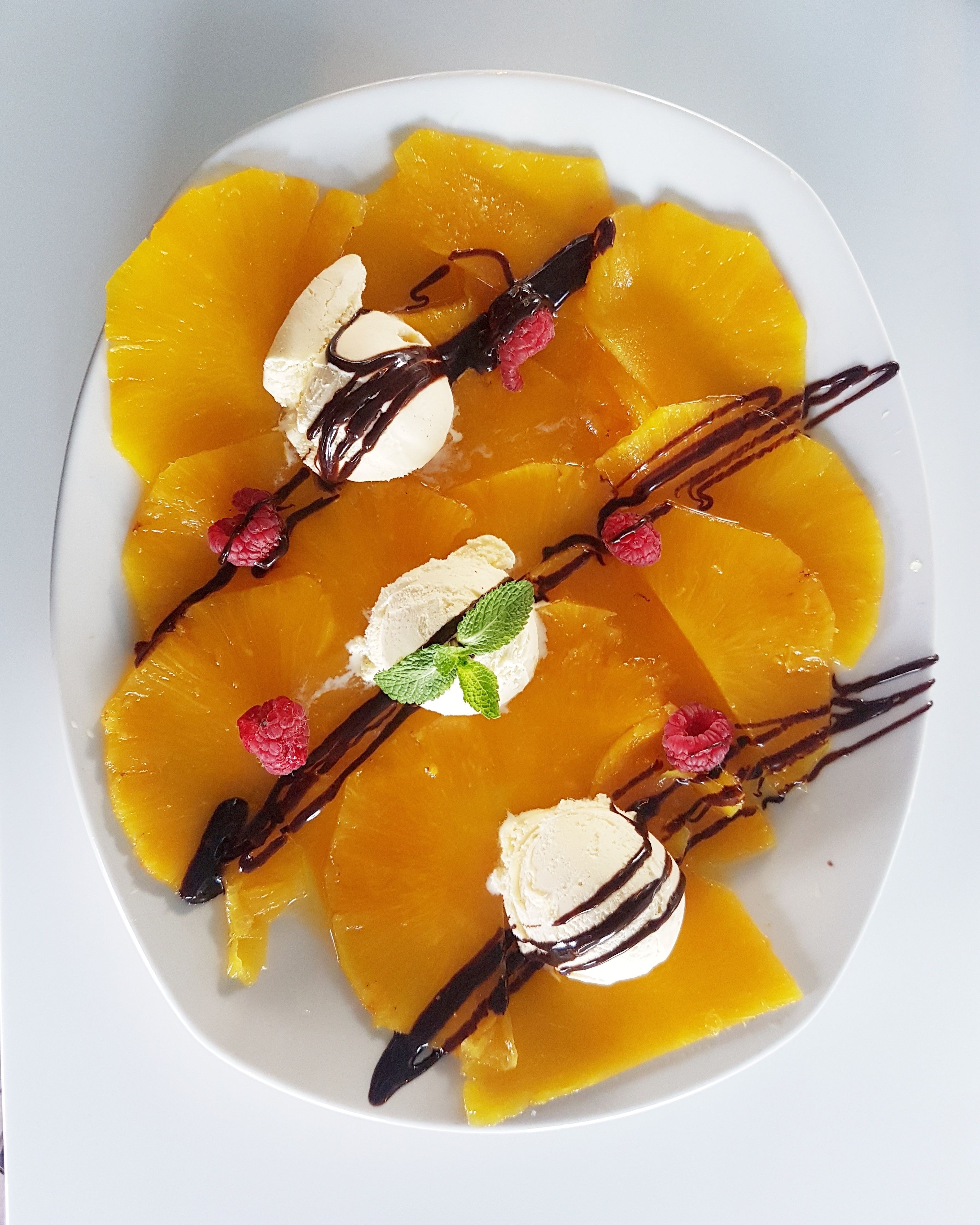 Un piatto dessert con spicchi d'arancia, cioccolato fuso, lamponi e foglie di menta.