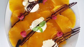 Un piatto dessert con spicchi d'arancia, cioccolato fuso, lamponi e foglie di menta.