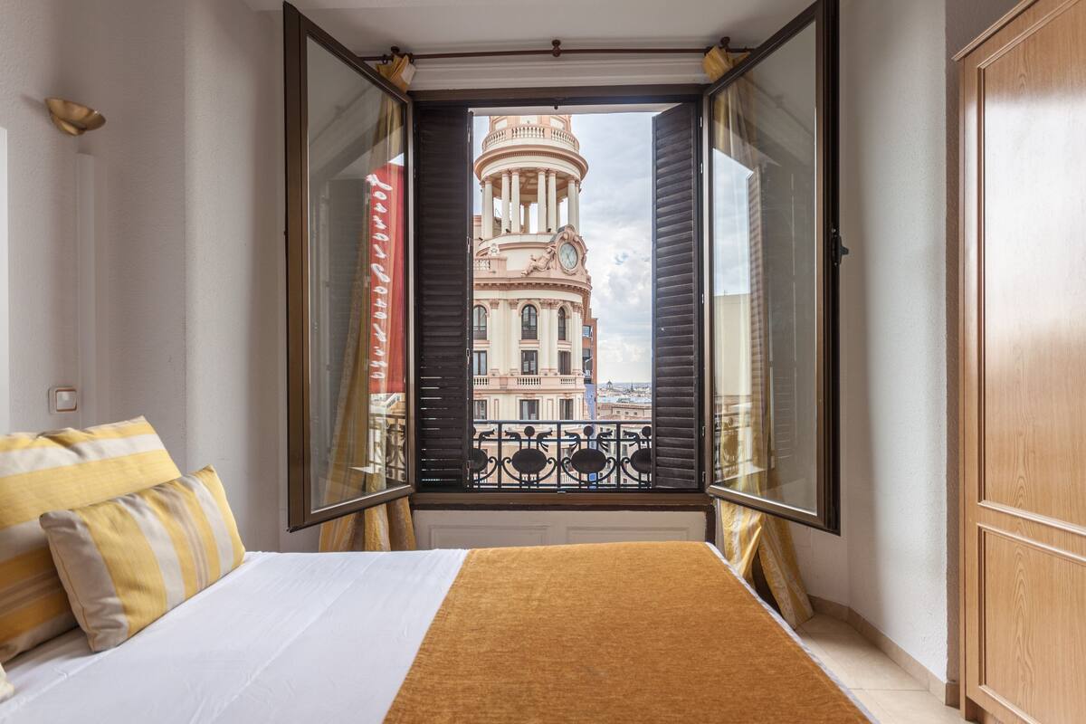 Un dormitorio con cama y ventana que ofrece vista a un edificio con columnas.