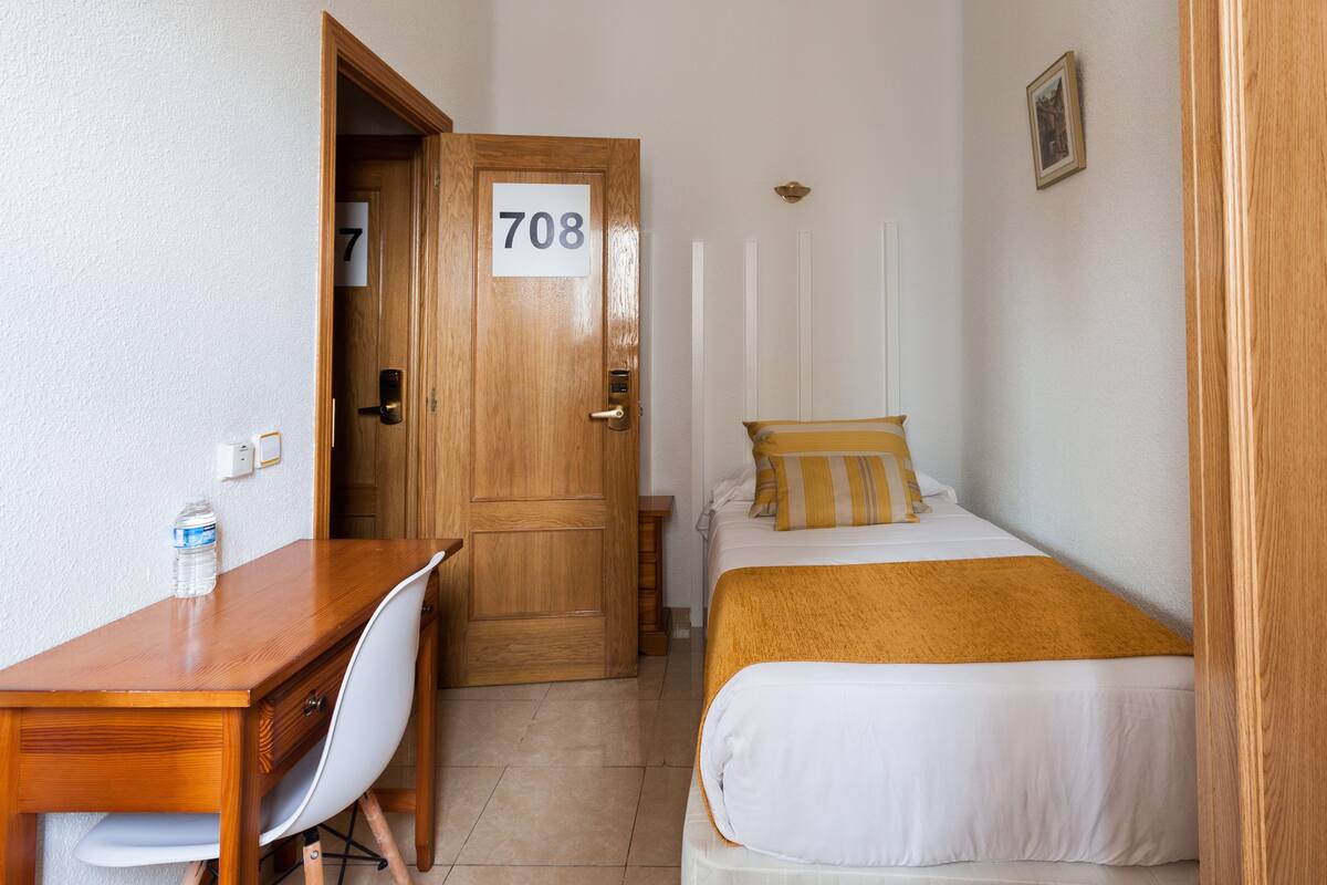 Una habitación de hotel con un escritorio de madera, una cama con almohada a rayas amarillas y blancas, y una puerta con el número 708.