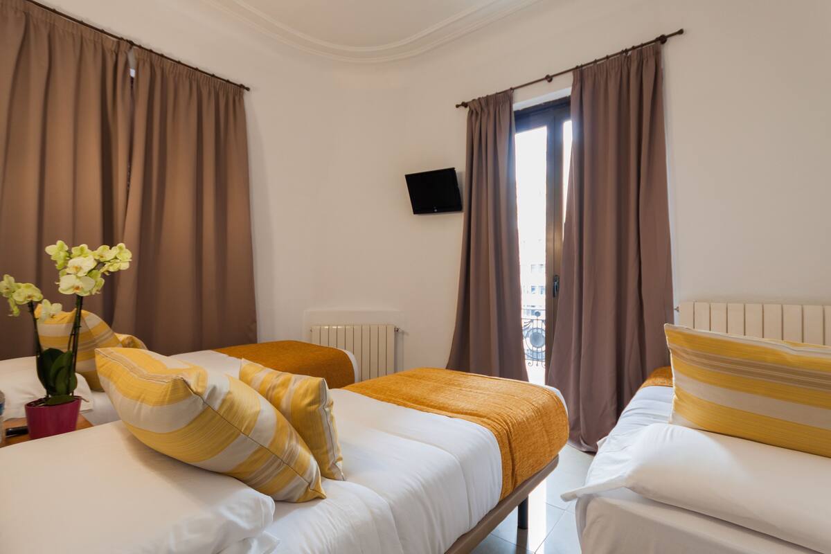 Habitación de hotel con dos camas, televisión y vista al exterior.