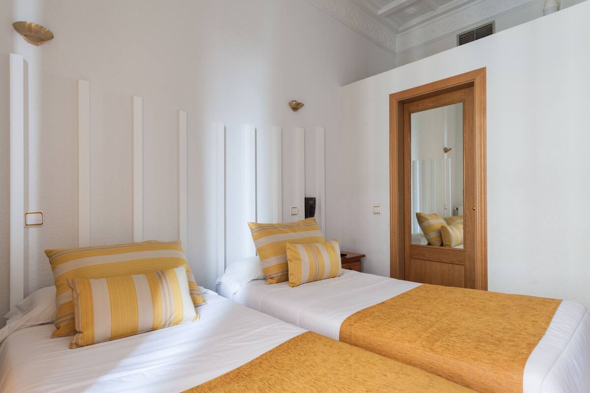 Habitación de hotel con dos camas, cada una con almohadas a rayas y una manta marrón.