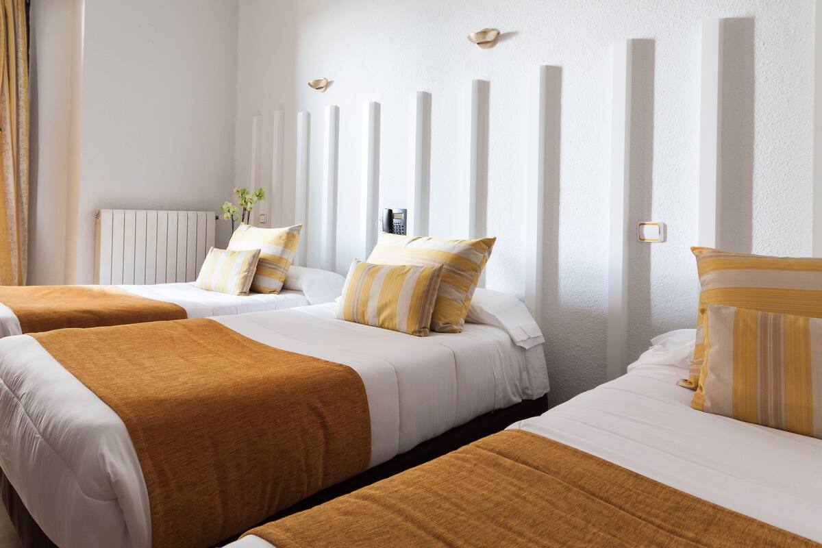 Una habitación de hotel con dos camas, cada una con una colcha blanca y marrón, y un cabecero blanco con paneles verticales.