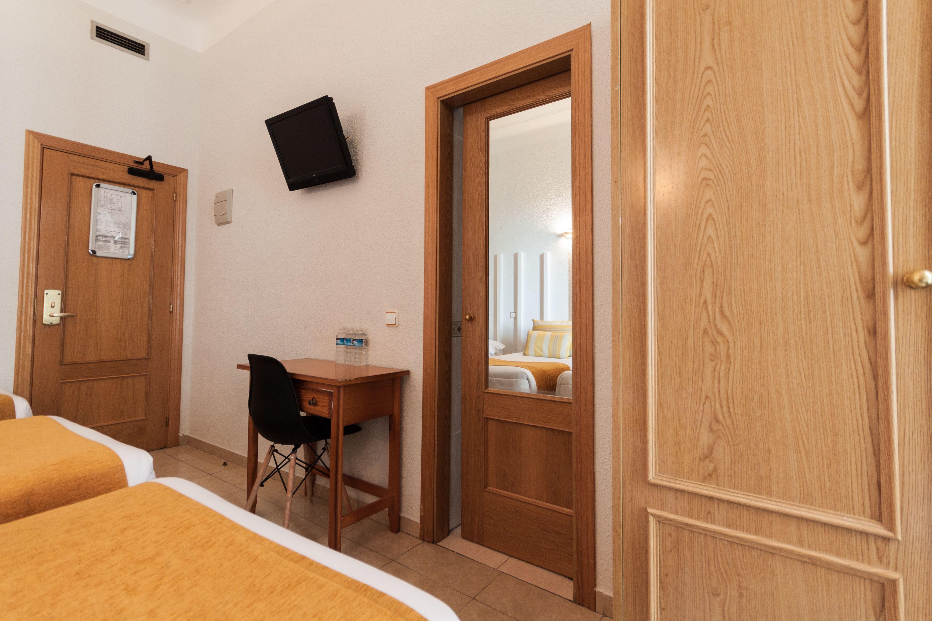 Ein Hotelzimmer mit zwei Betten, einem Schreibtisch, einem Stuhl, einem Fernseher und einer Tür zu einem Badezimmer.