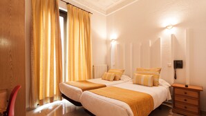 A hotel room with two beds, a wooden nightstand, a red chair, and a window with yellow curtains. - Hostal Josefina (Madrid)
