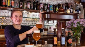 Un bar con una variedad de botellas y copas, una bandeja con postre y un jarrón con flores.