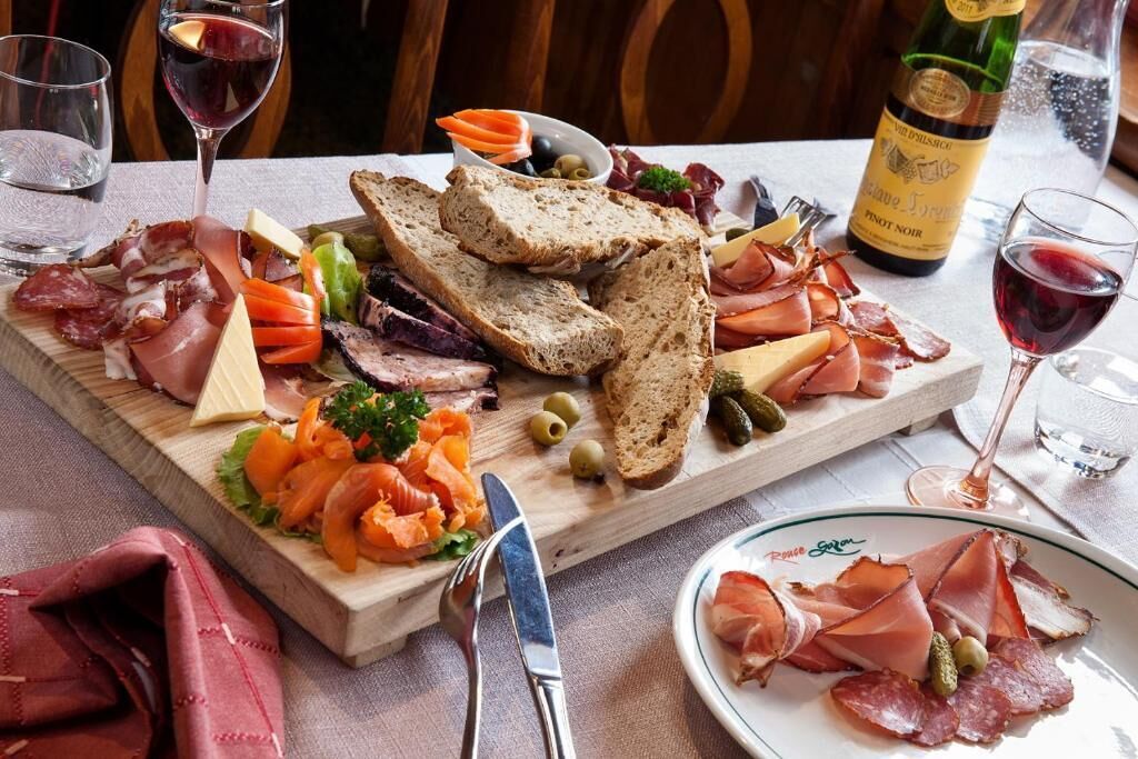 A charcuterie board with various meats, cheeses, and vegetables, accompanied by wine glasses and a bottle of wine.