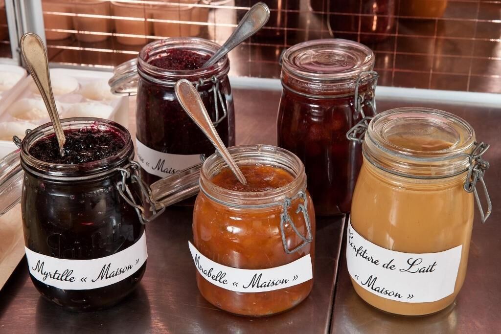 Four glass jars with metal clasps and labels, containing different types of preserves, placed on a wooden surface.