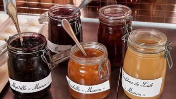 Four glass jars with metal clasps and labels, containing different types of preserves, placed on a wooden surface.