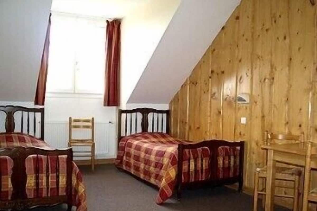 A room with two beds, wooden walls, a window with curtains, and a small table.