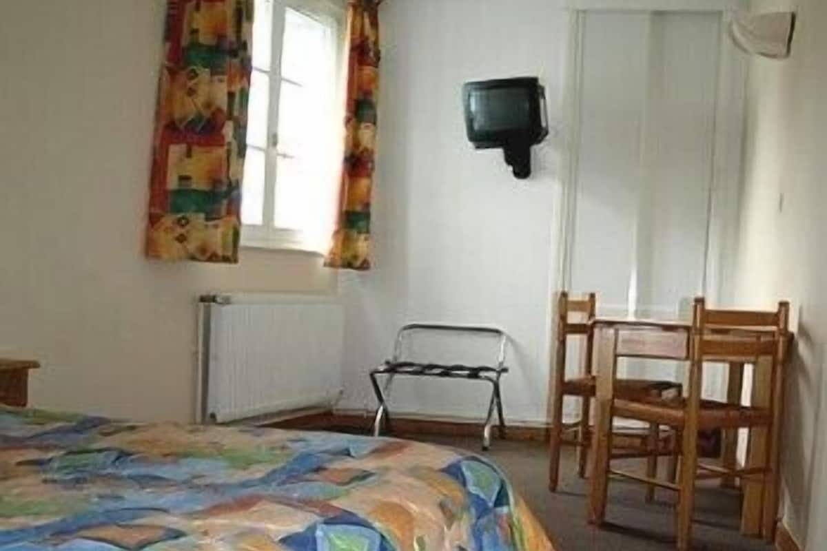 A bedroom with a bed, a chair, a radiator, and a television mounted on the wall.